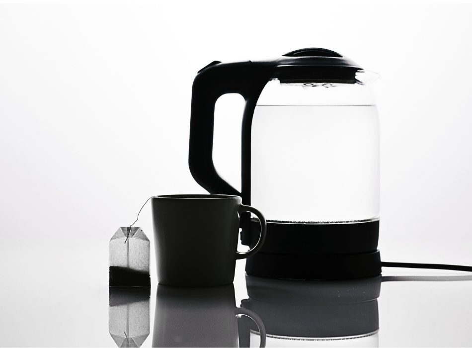 A transparent electric kettle and cup of tea with a dangling tea bag stand out sharply against a white background.