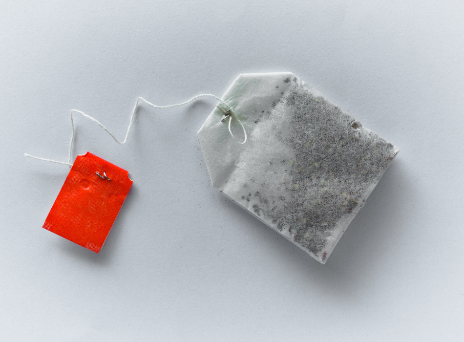 A tea bag with a red label on a string sits on a white surface.