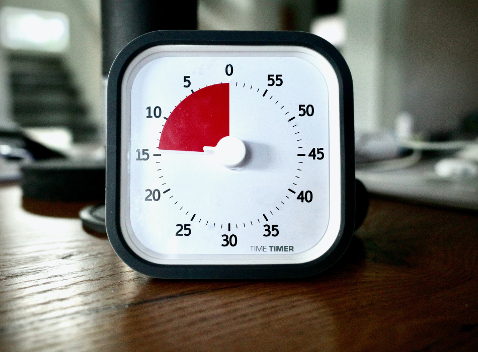 A square kitchen timer sits on a wooden surface, with the timer set at 15 minutes.