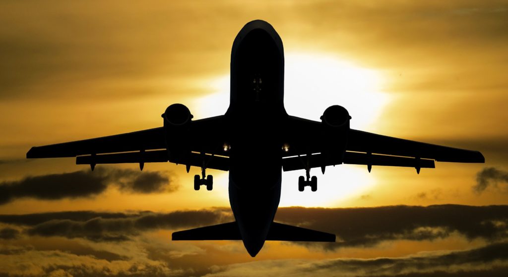 A large passenger plane takes off. Its silhouette stands out against a yellow background of setting sun and clouds.