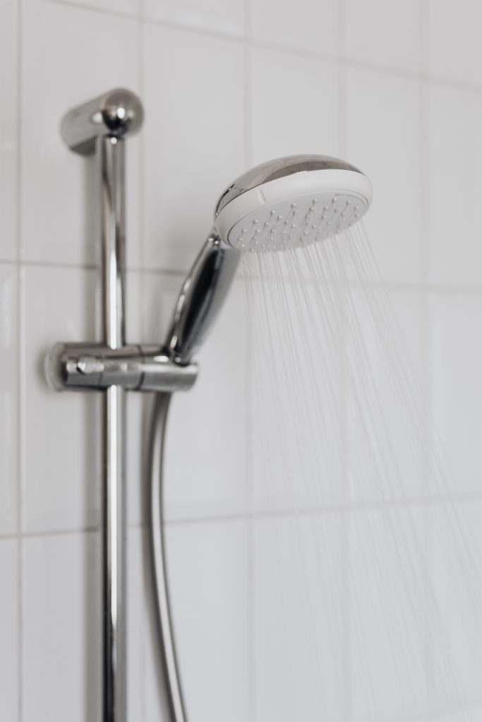 A round plastic showerhead sprays water downward against a background of white tiles.