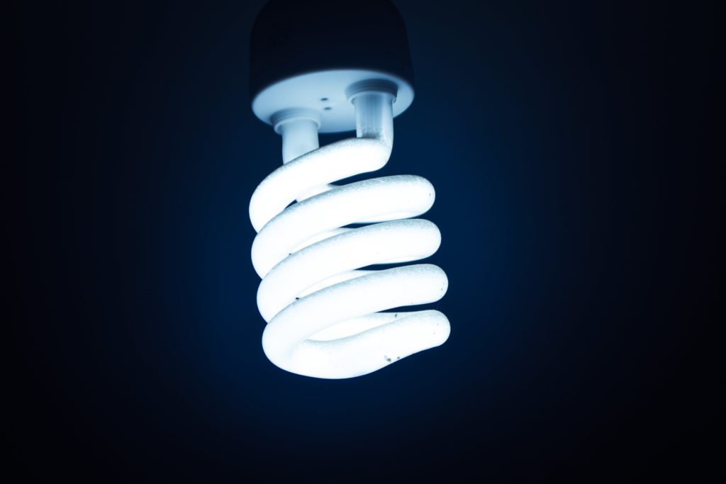 A bright white CFL light bulb hangs upside down, standing out against a navy blue background.