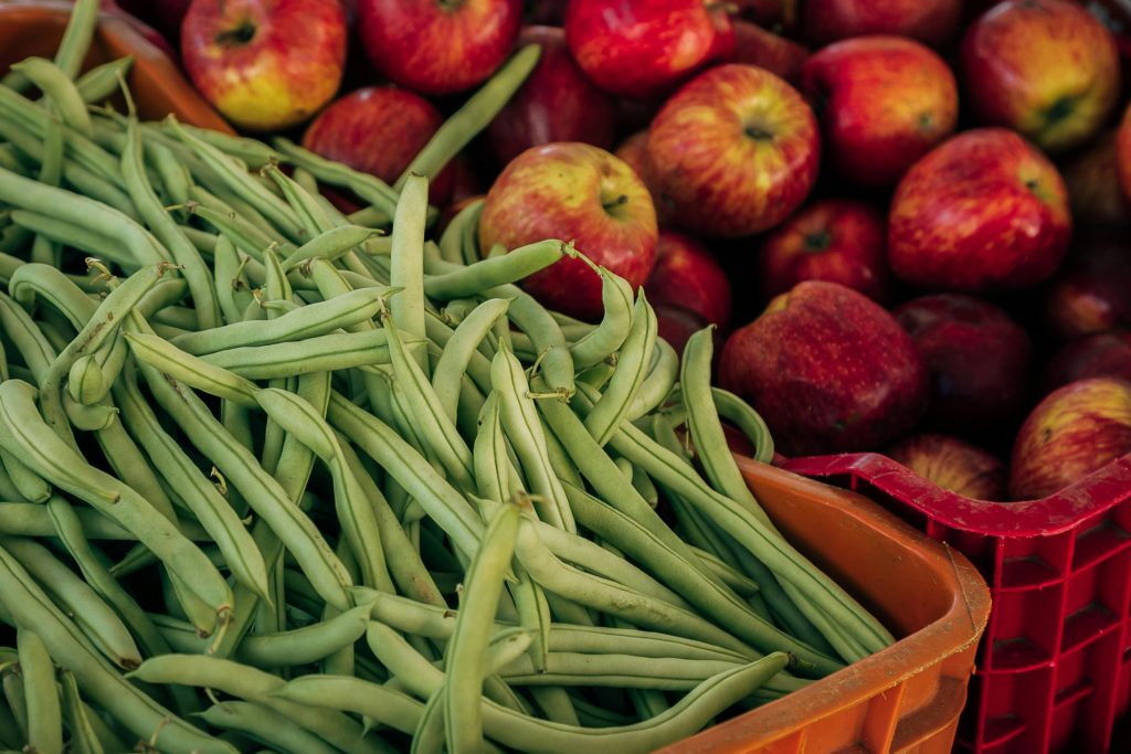 A heaping basket of green beans sits next to a basket of apples.