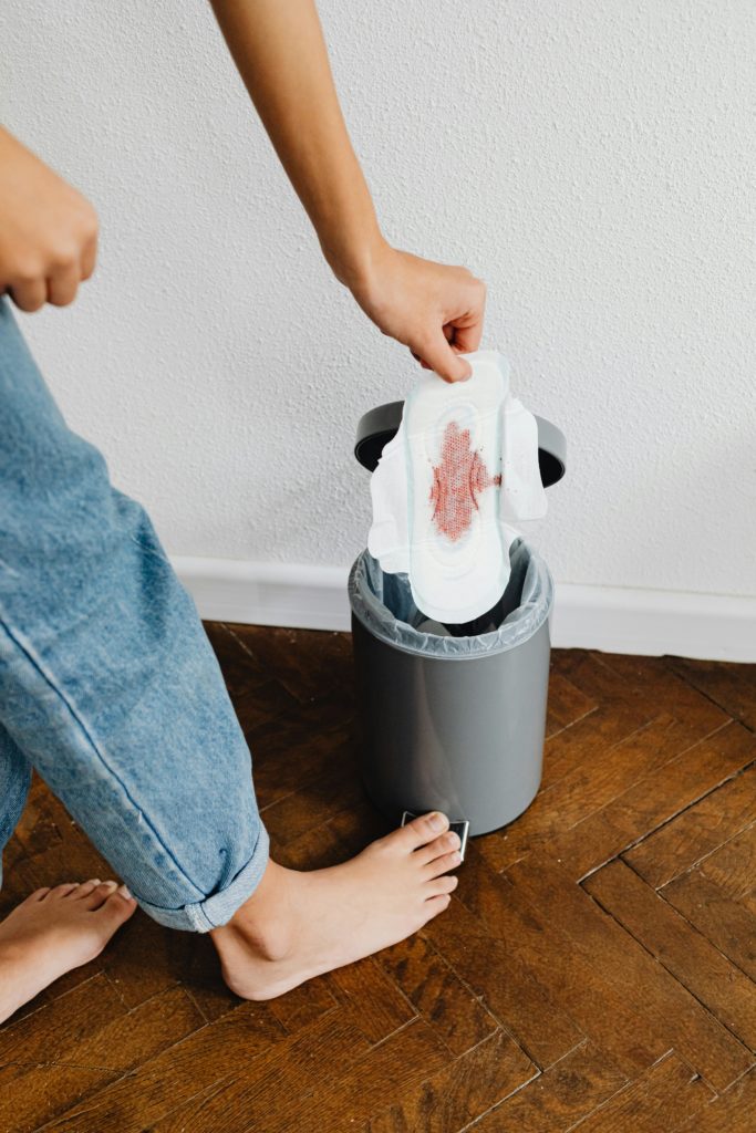 A woman wearing jeans drops a used disposable menstrual pad into a mini garbage can.