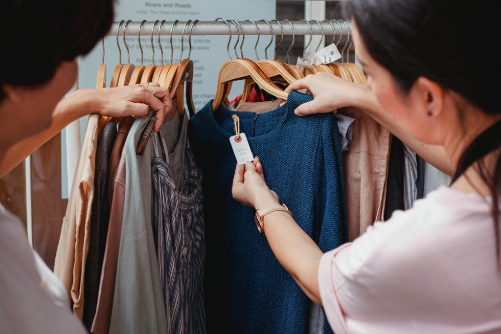 A woman checks the price tag on a blue sweater hanging on a clothes rack.