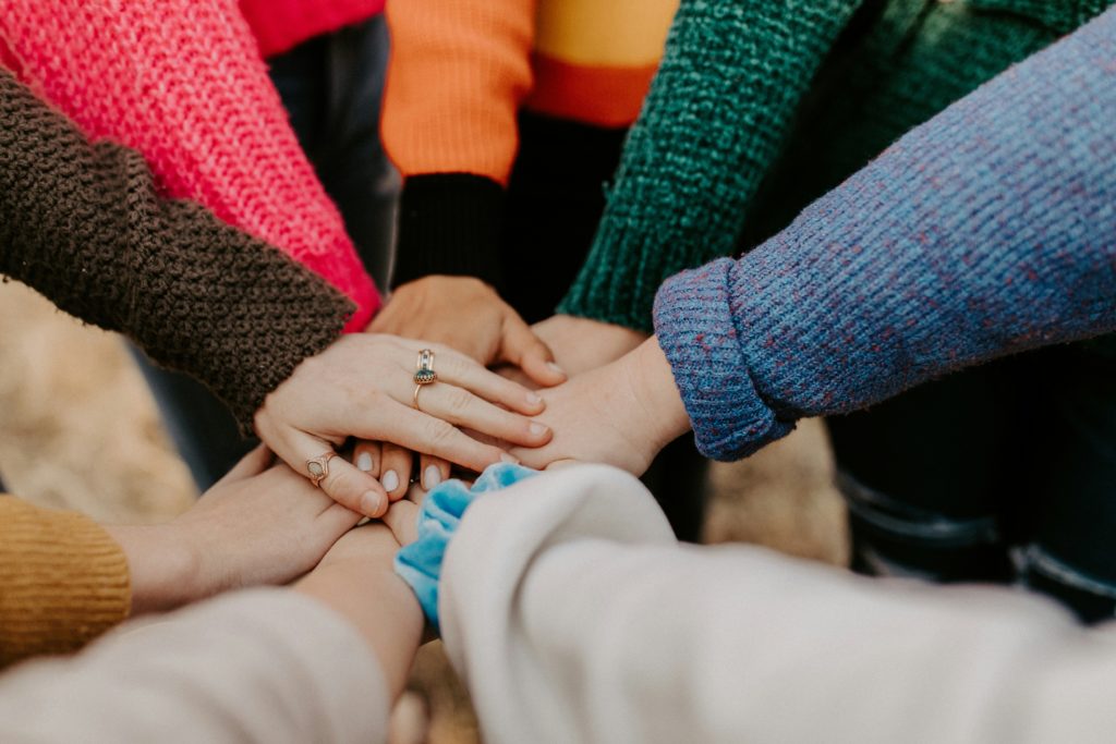 A group of people wearing colourful sweaters put their hands together.