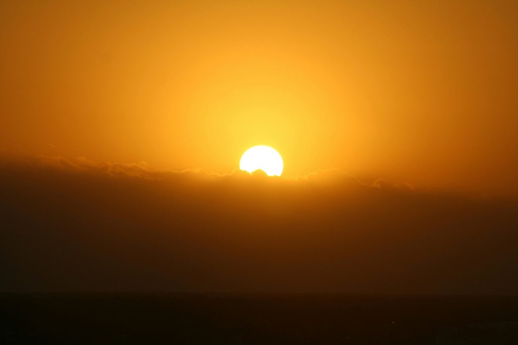 A bright sun sets behind dark clouds, casting the sky orange.