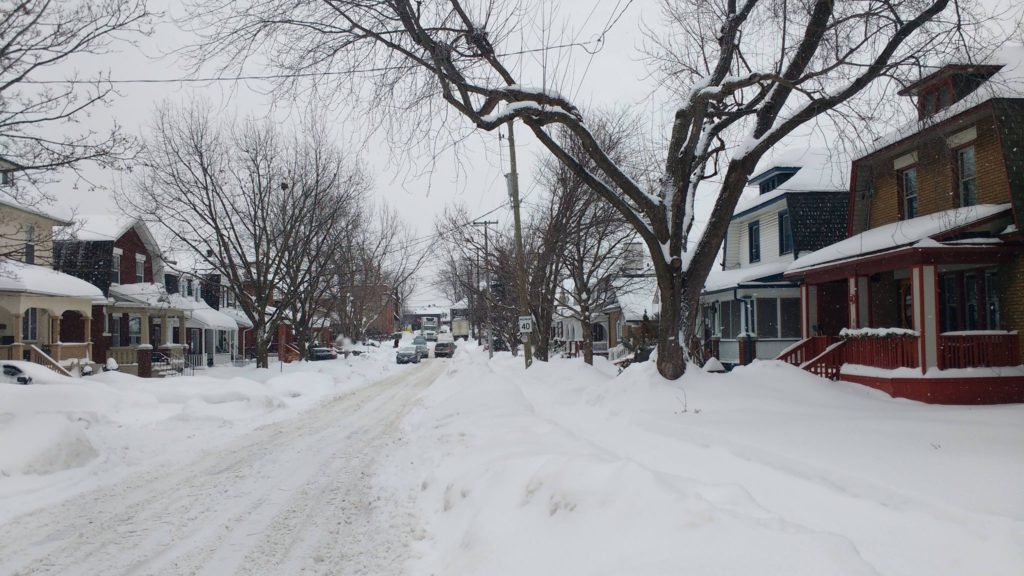 A snowy residential street with prominent snowbanks and piles of snow.