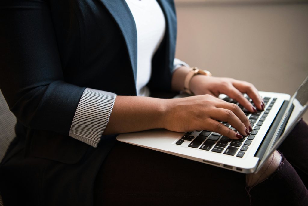 A woman wearing a navy blue blazer types on the keyboard of a MacBook.