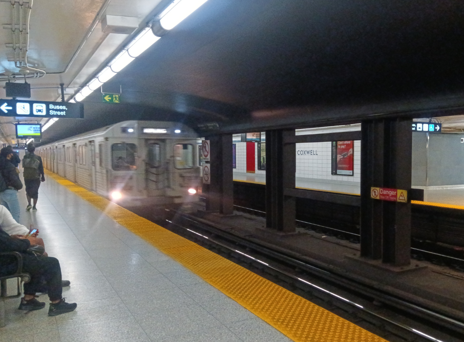 A silver subway train pulls up to a platform, its headlights flashing.