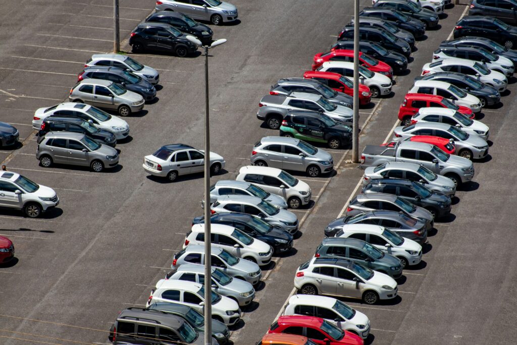 A parking lot with rows of white, grey, red and black cars.