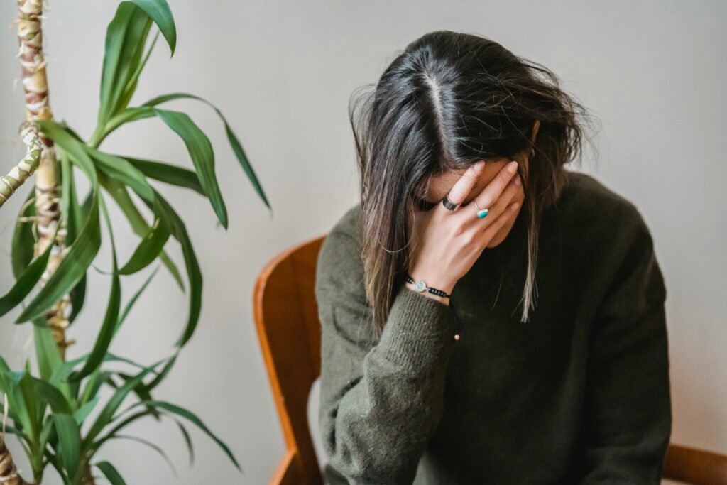 A woman with dark hair wearing a dark-green sweater rests her face in her hand.