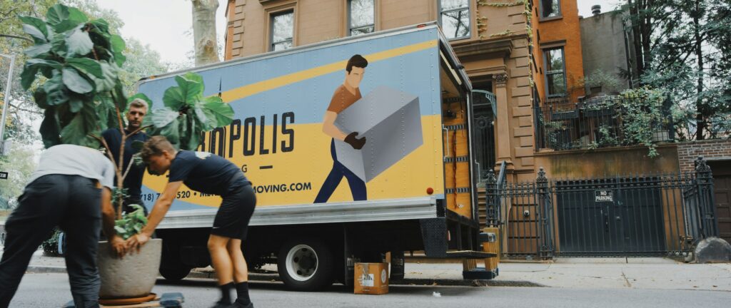 Three men move a large potted plant in front of a moving truck