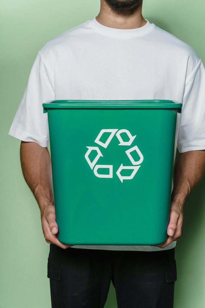 A man wearing a white t-shirt holds a green mini recycling bin.