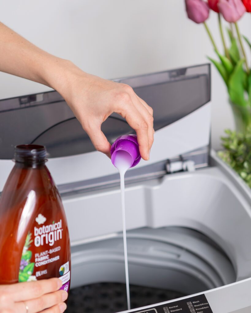 A person pours detergent from a purple cap into a washing machine.