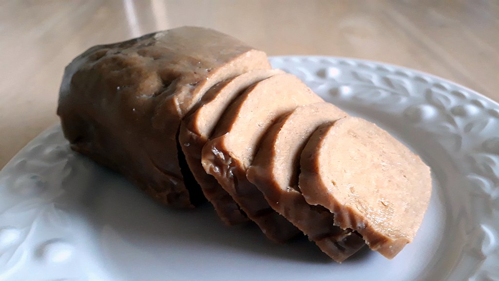 A loaf of seitan on a plate, with some pieces sliced off.