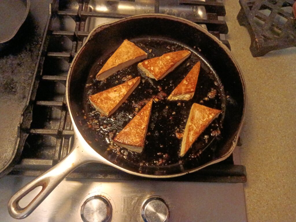 Triangles of tofu fry in a cast iron frying pan.