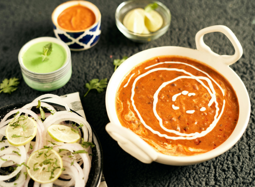 A bowl of red lentil curry sits next to a bowl with onion slices.