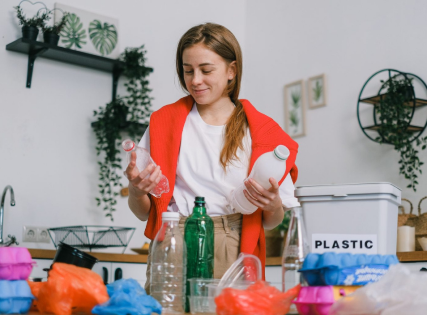 A woman holds a plastic bottle in each hand with more plastic containers on the counter in front of her.