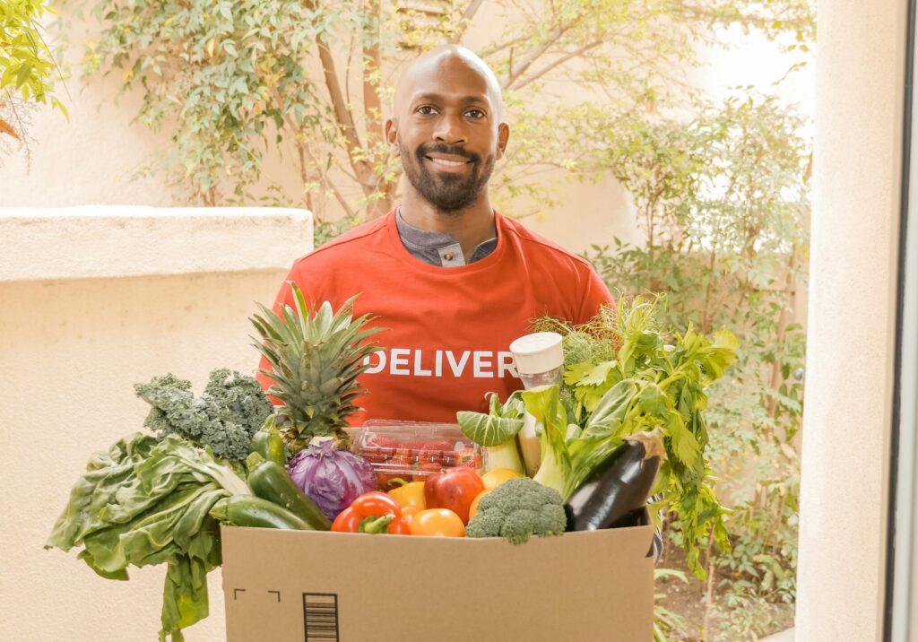 A delivery man carries a cardboard box full of produce.