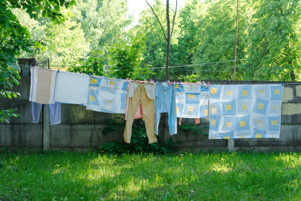 Laundry hangs on a clothesline in a green backyard.