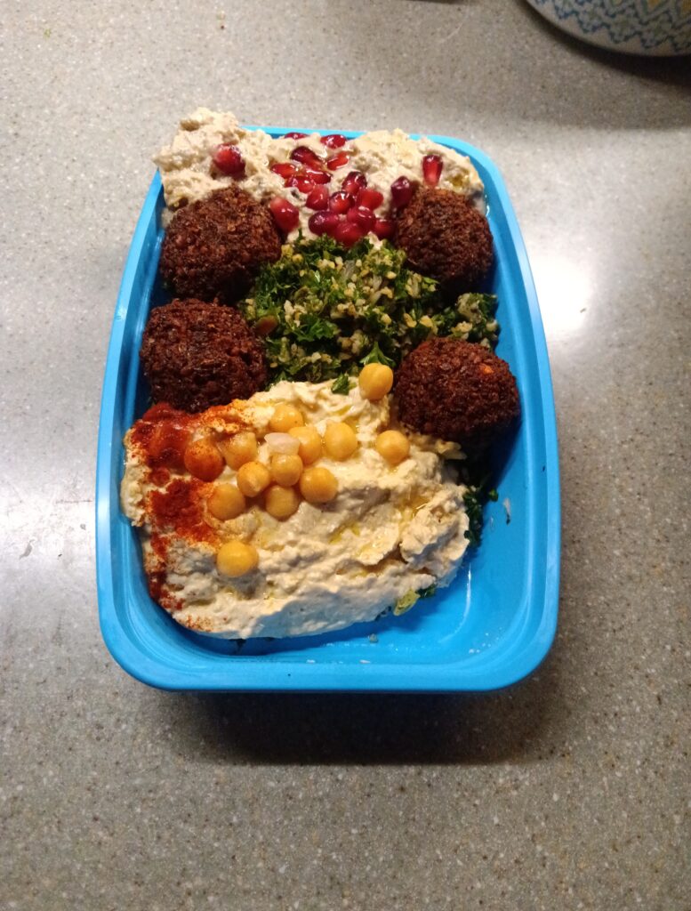 A blue plastic container containing falafels, salad and dips.