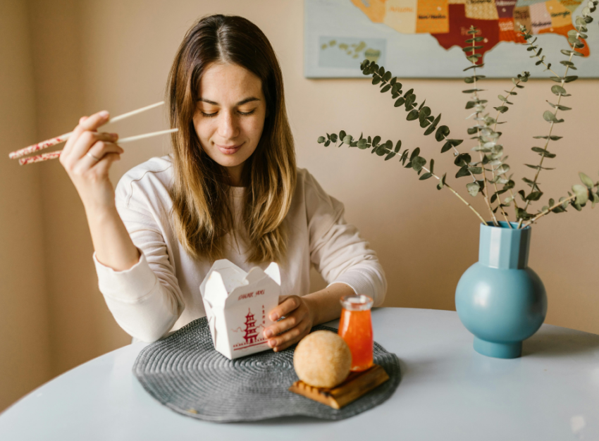 A woman holds chopsticks over a paper takeout box.