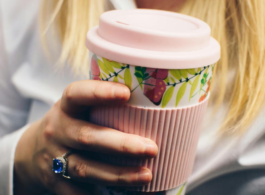 A woman holds a pink reusable coffee cup with a berry pattern.